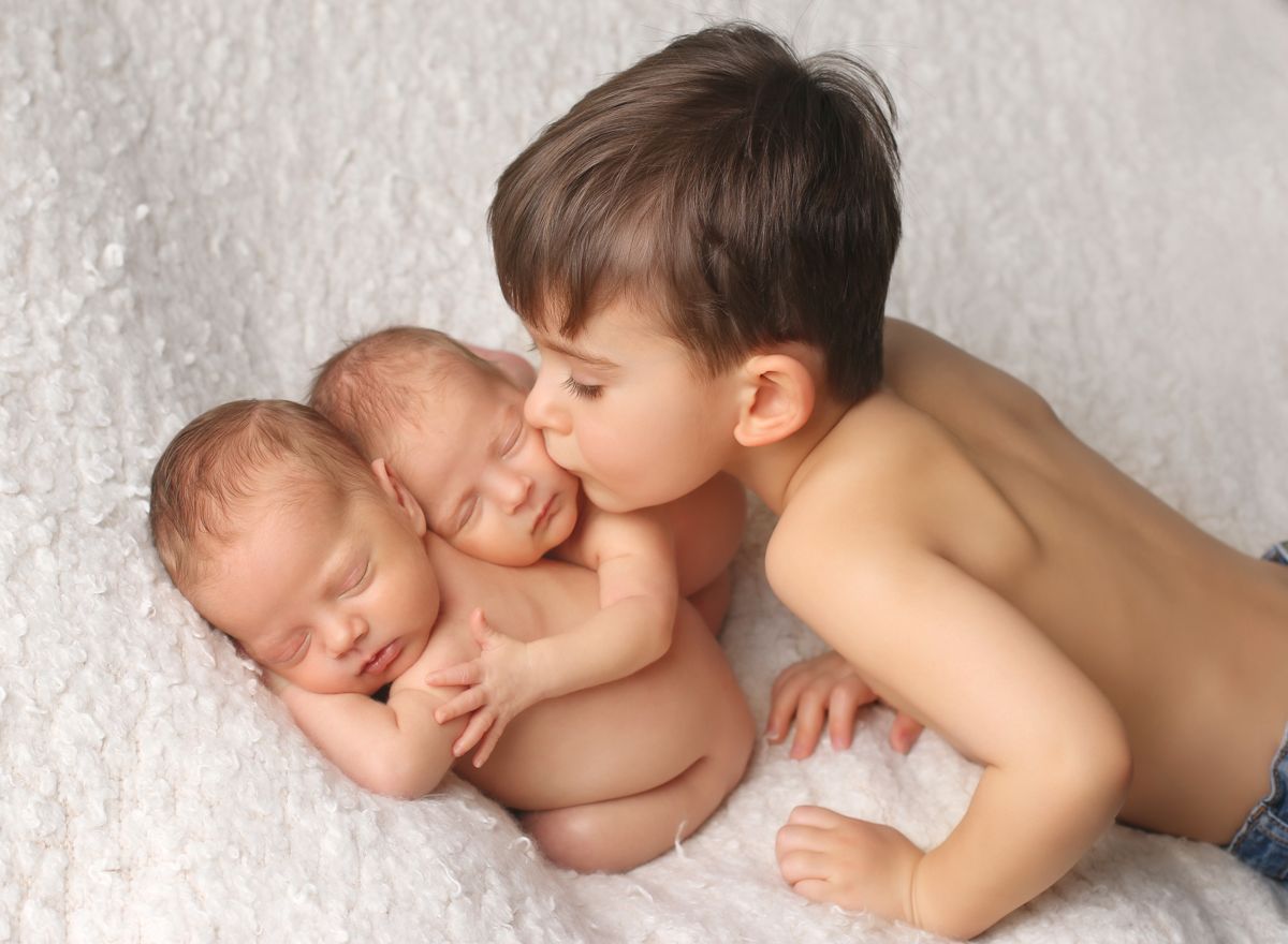 Starší bráška zdraví novorozená dvojčátka na newborn fotografii z ateliéru