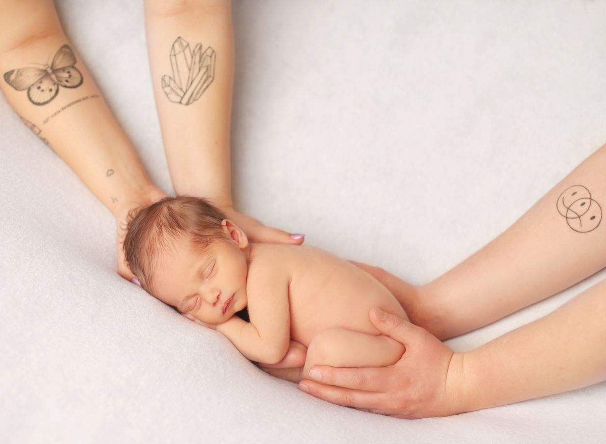 Ruce rodičů drží spící novorozené miminko na přirozené newborn fotografii