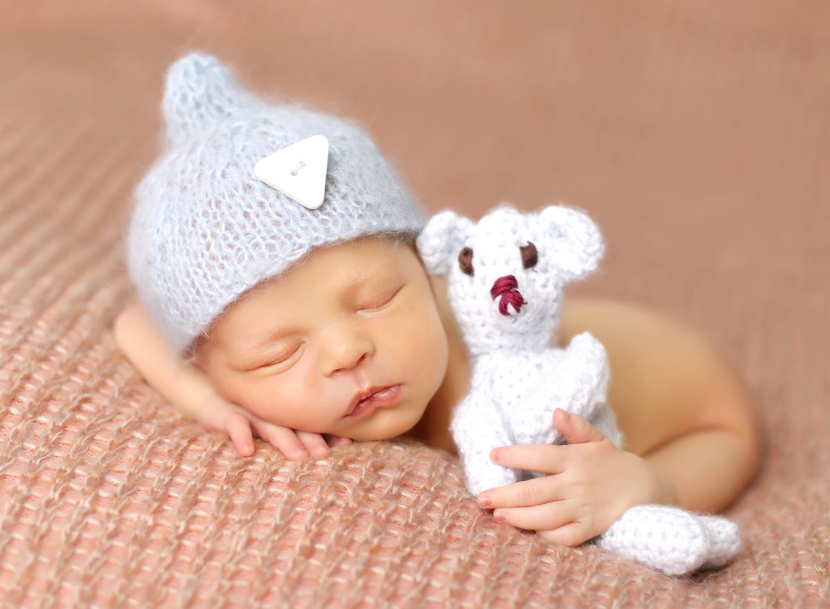 Novorozené miminko spí v pletené čepičce s háčkovaným medvídkem v ruce