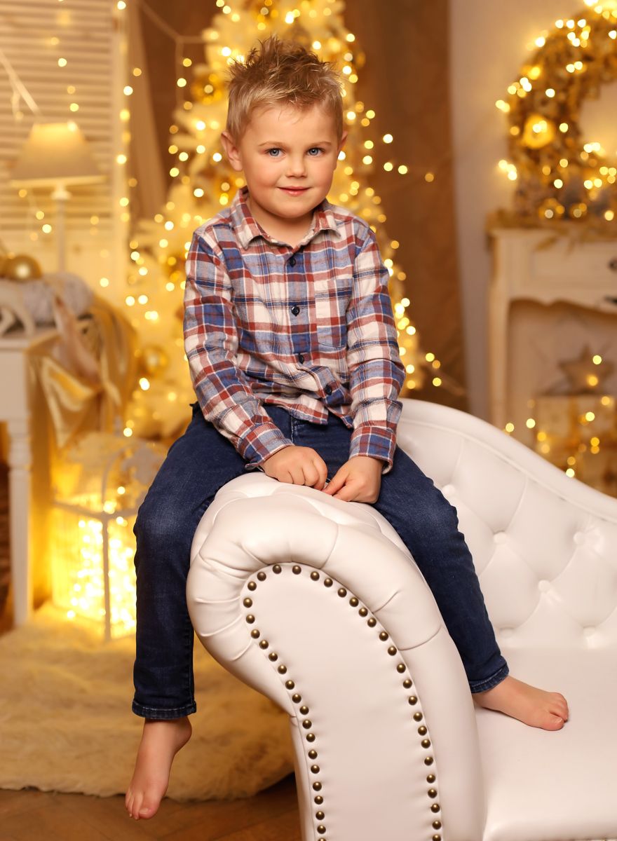 Malý kluk sedí před vánočním stromkem na ateliérové fotografii