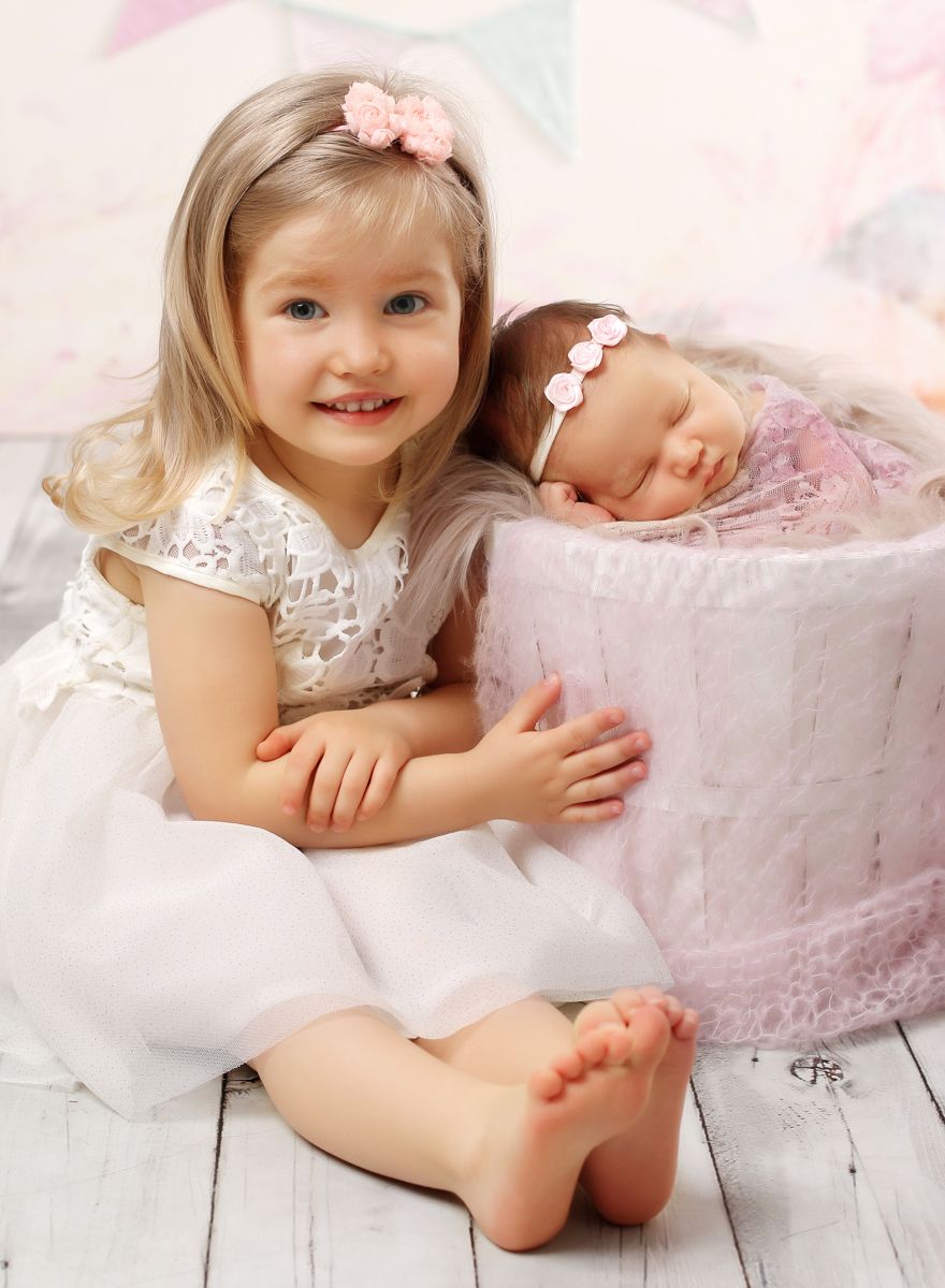 Newborn fotografie novorozeného miminka vedle kterého sedí starší sestřička