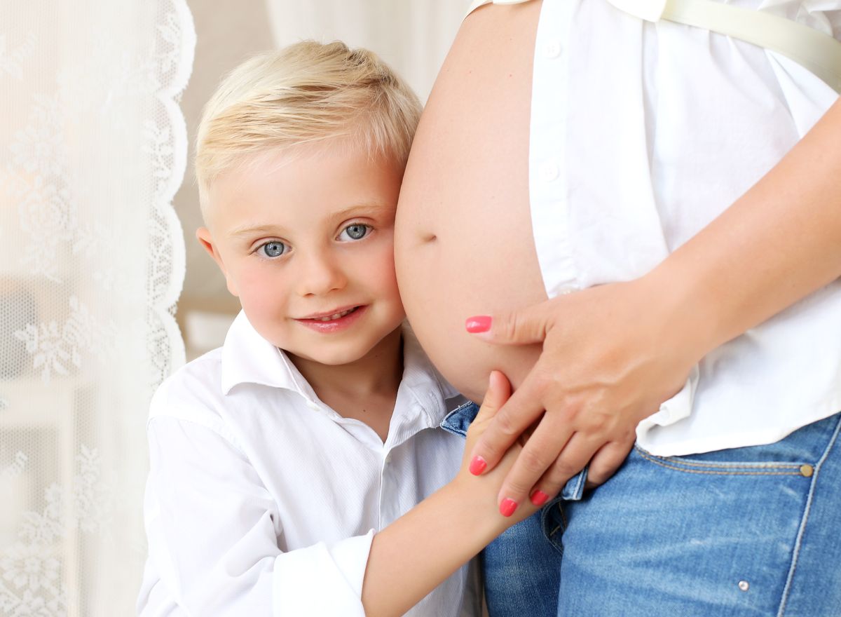 Starší dítě objímá těhotenské bříško a poslouchá nenarozené miminko