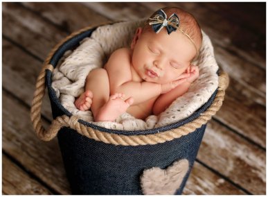 Novorozené miminko vyfotografované spící v modrém textilním kyblíčku s čelenkou a rukama pod hlavou