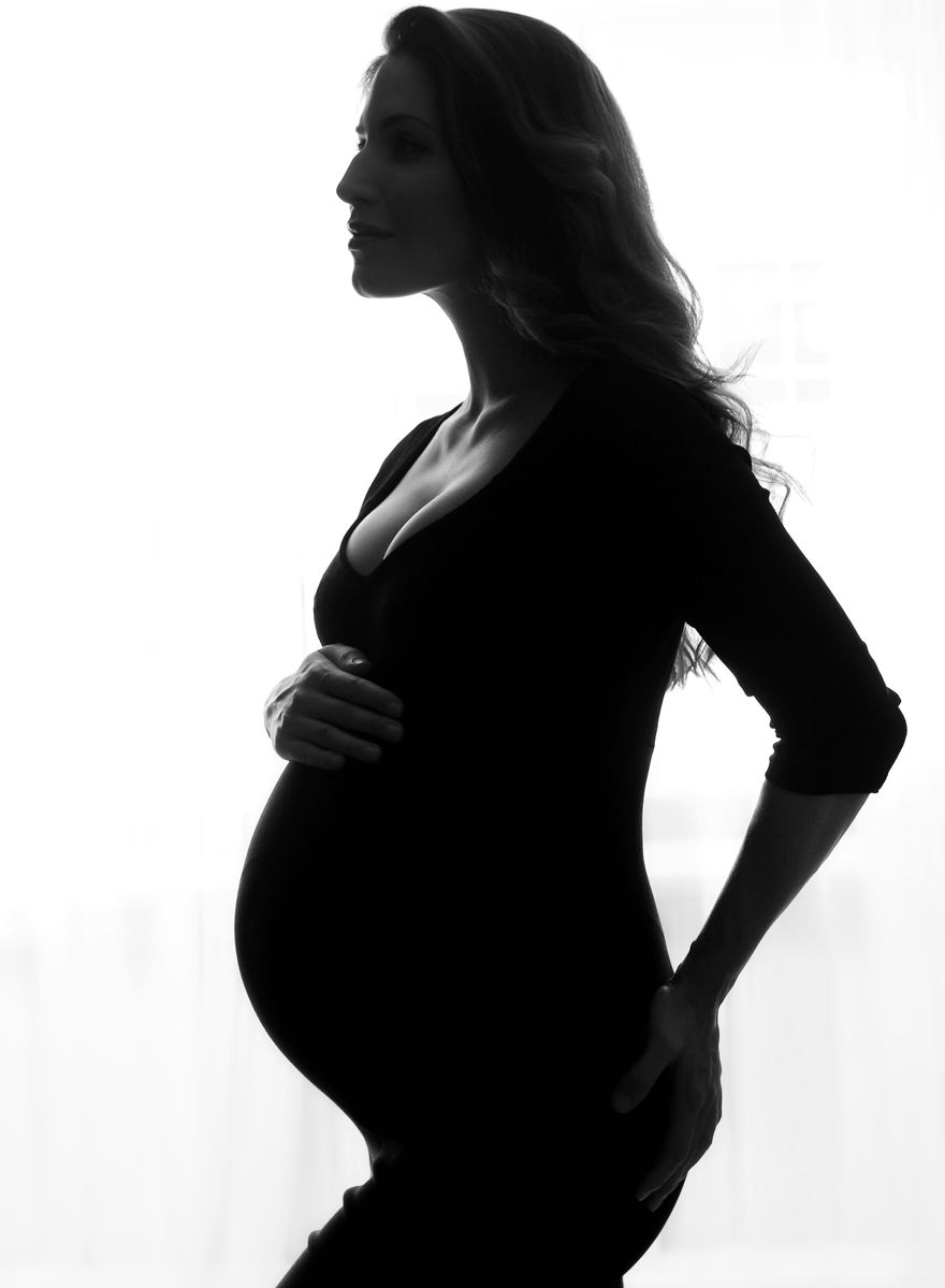 Černobílá boudoir fotografie stojící těhulky z profilu bříška se zadním světlem